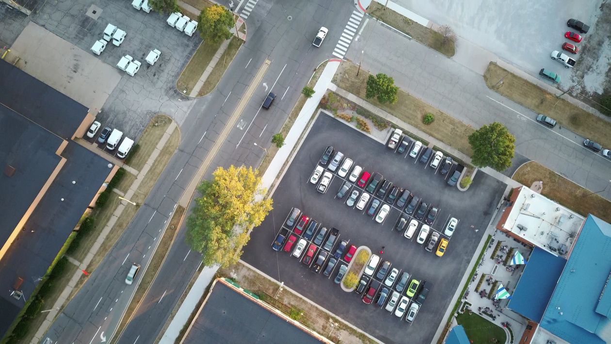 Drone shot of an urban parking lot and surrounding roads at daytime.
